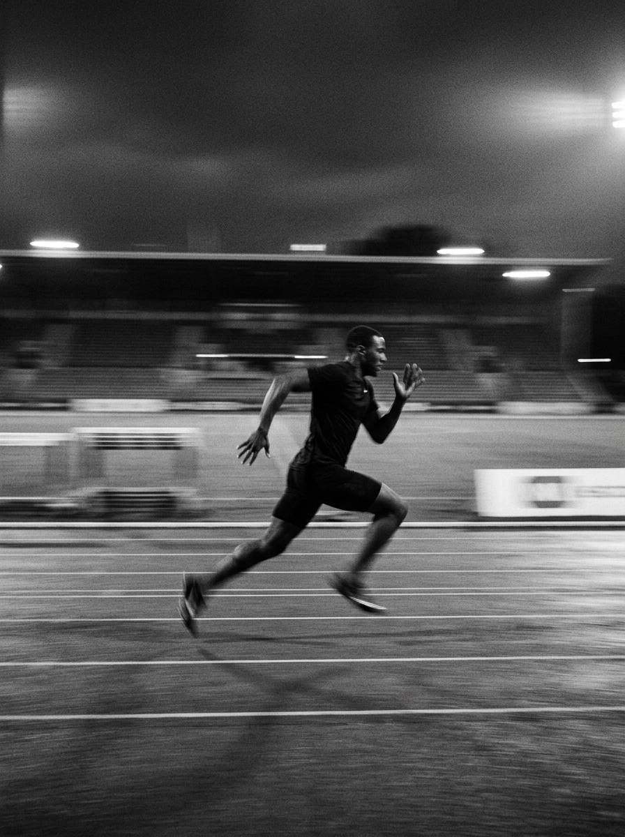Sprinteur lancé sur une piste d’athlétisme de nuit, en noir et blanc, filé horizontal