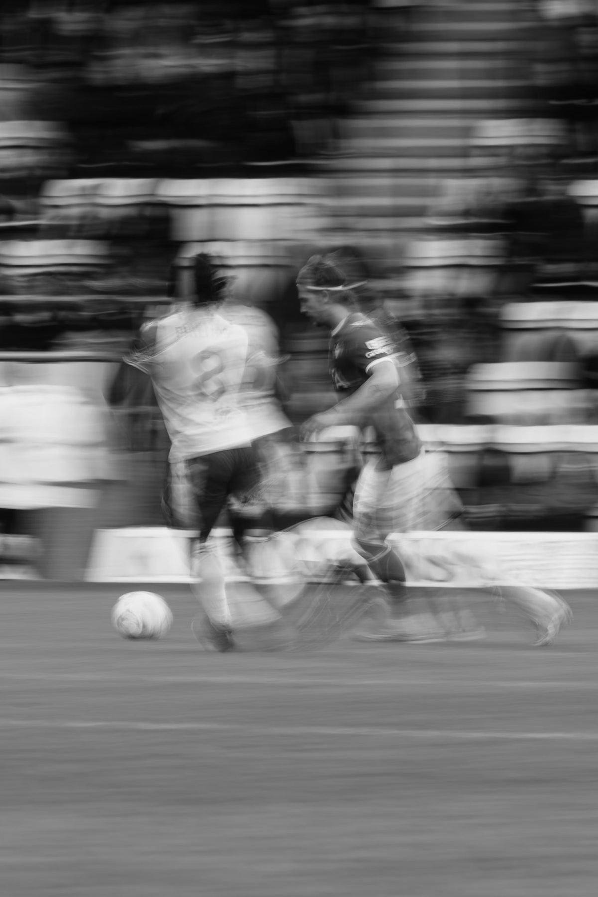 Deux footballeurs à la course derrière le ballon, photographiés en filé devant une tribune